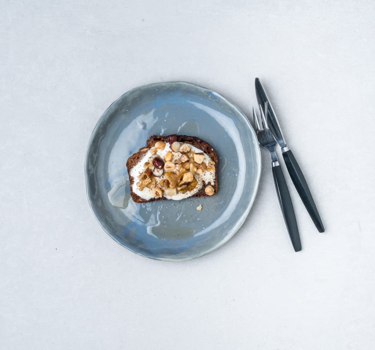 Blå tallrik med rostad macka med grekisk yoghurt toppad med nötter och honung.