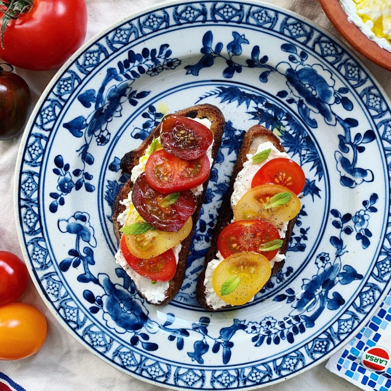 Blå och vit tallrik med rostat bröd, toppad med fetaost spread och tomater.