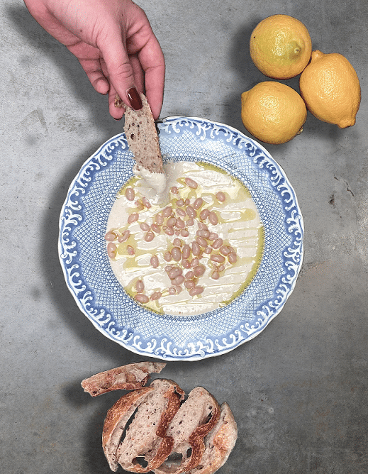 Böndippa med yoghurt, en hand som doppar ett bröd i dippen, tre citron vid sidan om.