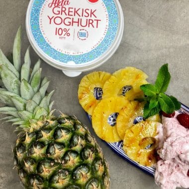 Grillad ananas och yoghurtglass med hallon och myntablad på toppen. Bredvid en hel ananas och Larsas äkta grekiska yoghurt.