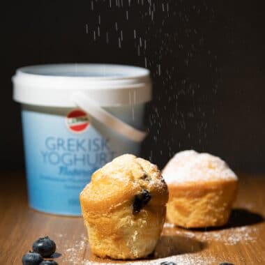 Yoghurtmuffins med färska blåbär och florsocker. Bakom muffinsen står en burk Grekisk yoghurt naturell från Larsafood.